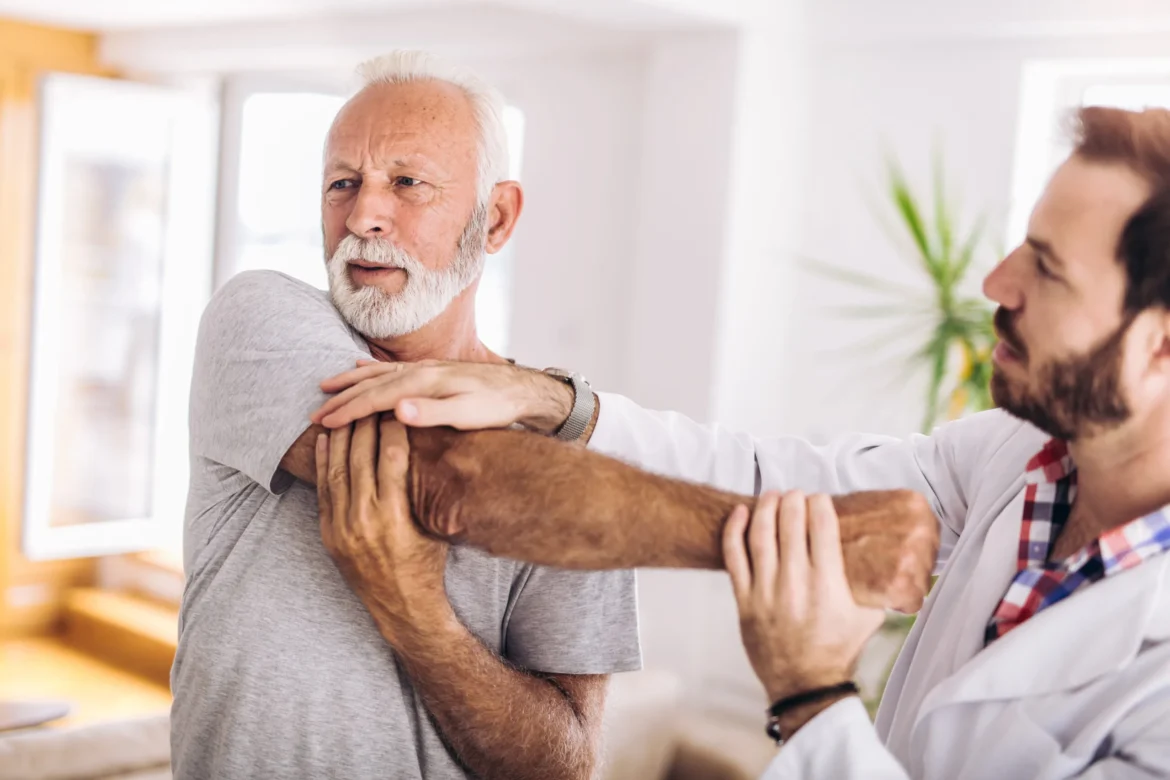 elderly man stretching out his shoulder and arm with the assistance of a physical therapist