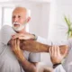 elderly man stretching out his shoulder and arm with the assistance of a physical therapist