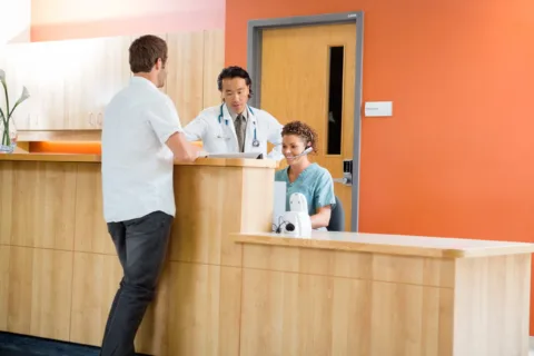 Doctor and nurse working at reception desk while patient standing in hospital