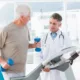 elderly man jogging on a treadmill holding weights while a doctor stands next to him