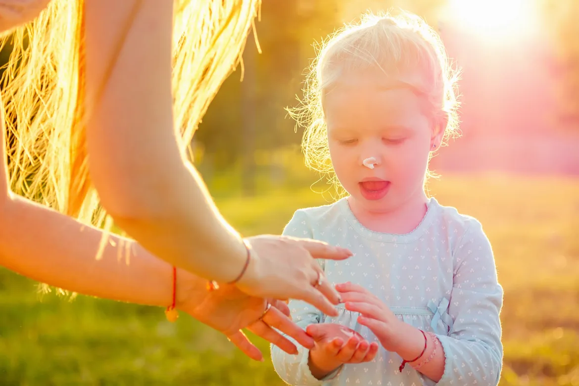 little girl applying sunscreen in a field