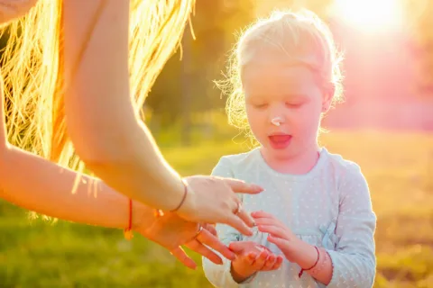 little girl applying sunscreen in a field